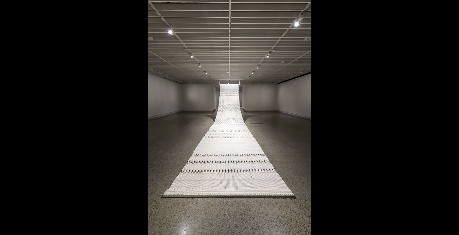 A large-scale artwork made of marine rope woven together, with various patterns, suspended from the ceiling and draping over the floor