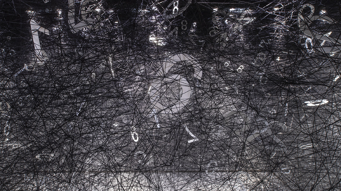 Black wool in a web stretched across a museum gallery floor, with white numbers sitting in random parts of it.