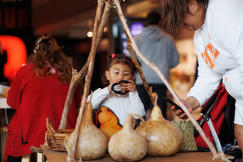 A young girl is inspecting a piece of card with mushrooms drawn on them. In front of her are some gourds with carving and marksings on them.