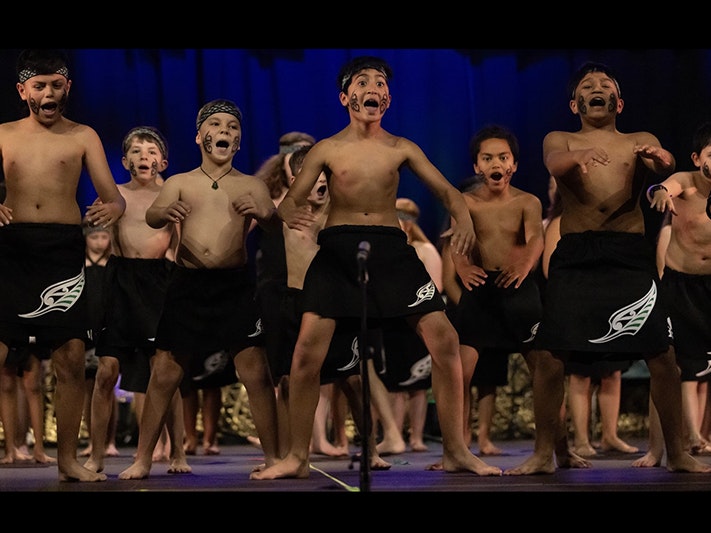 Photo courtesy of Whānau Manaaki Kindergartens Several young boys are performing kapa haka dance on stage.