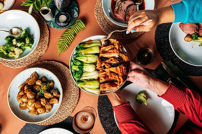 Photo taken by Anna Briggs. Te Papa (262593) A top-down photo of hands holding a dish of food, with another person using a fork to take something off the plate.