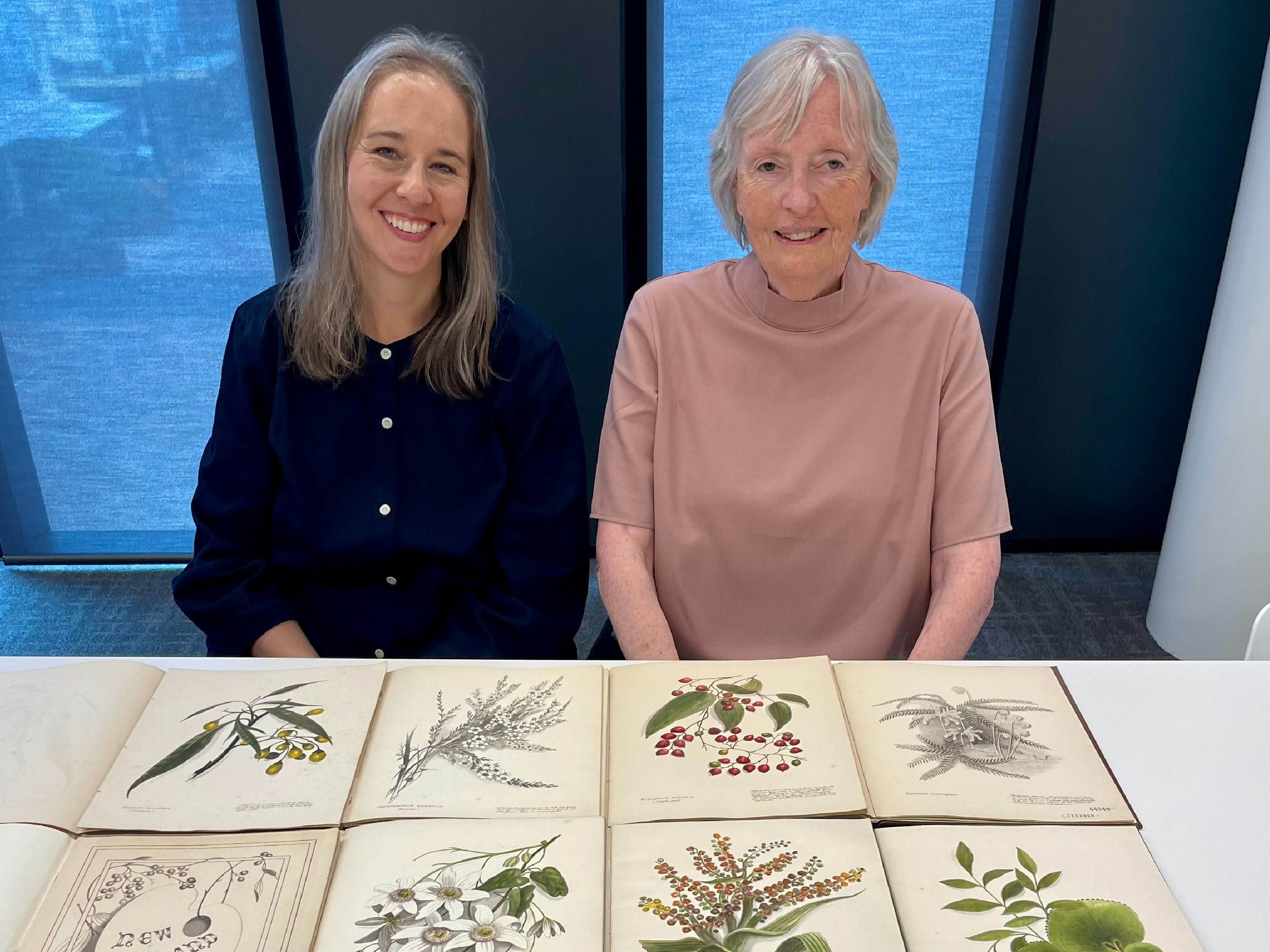 Catherine and Michele. Two women sit at a table with botanical illustrations of native new zealand plants spread out..