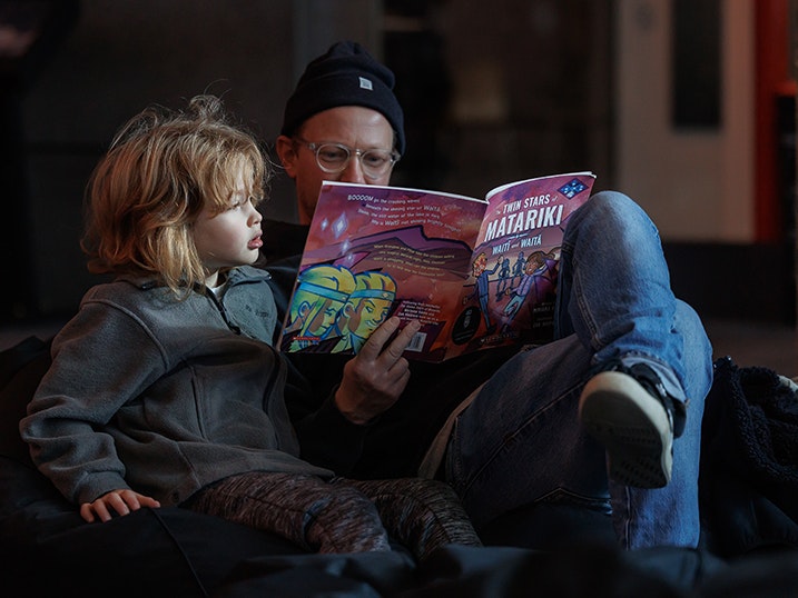 Matariki Whānau Day 2025 Te Papa. Photo by Jo Moore. Te Papa (268687) An adult is reading a book about Matariki to a child.
