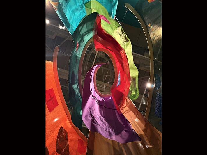 ‘Āiga hanging in PlaNet Pasifika. Te Papa Looking up at a ceiling through several coloured banners hanging in a spiral.
