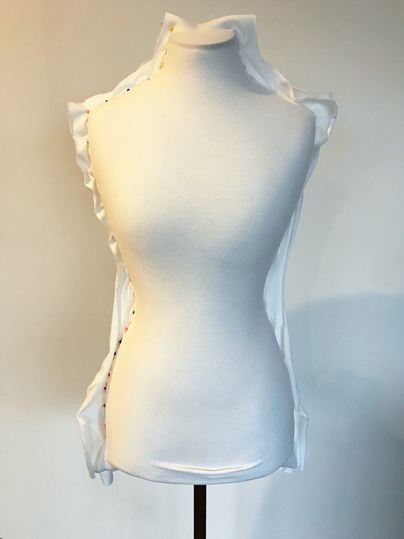 A dressmaker's dummy with material pinned to the back of it.