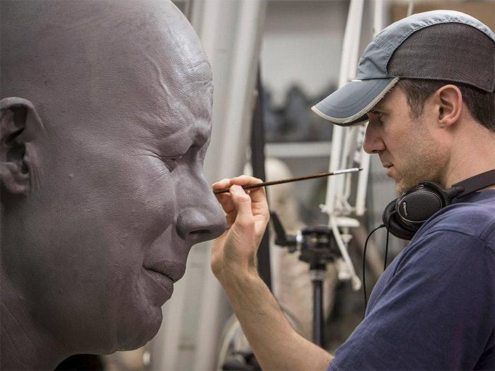 A man works on one of the giant model's faces.