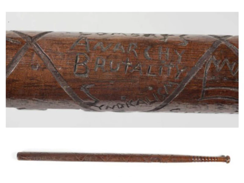 A closeup photo of inscription on a wooden baton, saying 'Combats anarchy, brutality, socialism'. The full baton is shown below.