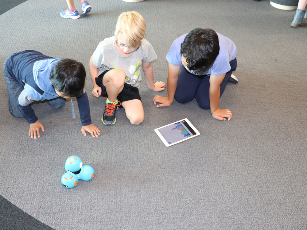 Three young children using a tablet and robot
