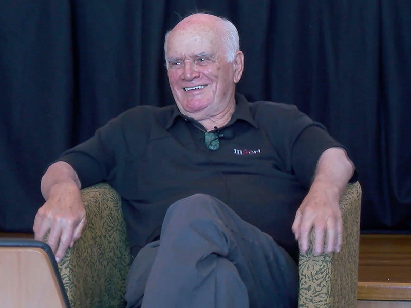 An older man sitting in a chair and laughing at someone off camera