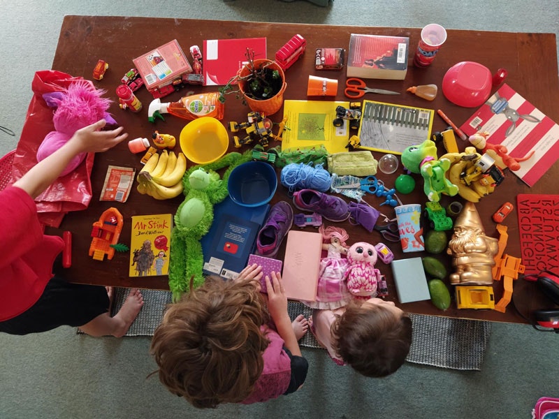 Three kids make a rainbow from toys and other household items