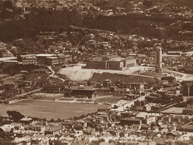 Vivienne Lee-Johnson at National Museum site, Buckle Street, Wellington, 1940s, Wellington, by Eric Lee-Johnson. Purchased 1997 with New Zealand Lottery Grants Board funds. CC BY-NC-ND 4.0. Te Papa (O.011045) Aerial view of the Basin Reserve, the Carillon, and the old Dominion Museum building