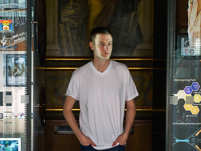 Portrait of Simon Denny standing near his exhibition titled Secret Power