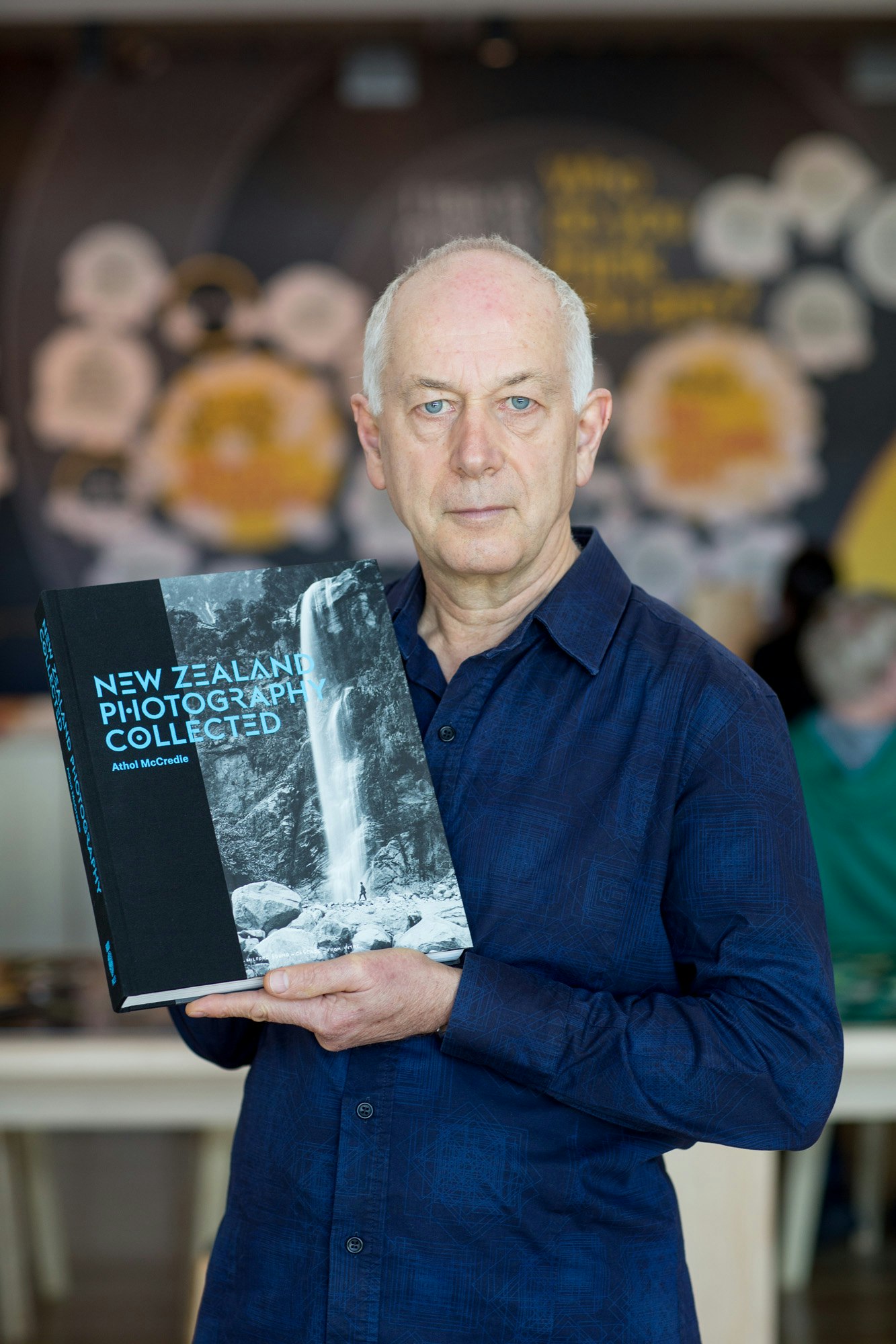 Author Athol McCredie holding a copy of his book, New Zealand Photography Collected.