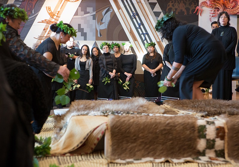 Ladies placing feathered cloaks over the boxes containing Māori remains