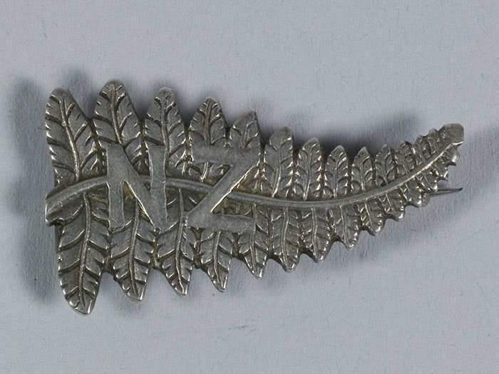 Brooch in the shape of a silver fern with the letters N and Z on it