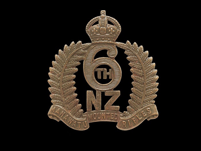 Cap badge featuring a wreath of two silver ferns, a crown, and the words 6th NZ Manawatu Mounted Rifles