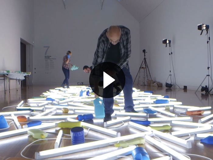 Still from the video 'Bill Culbert installing 'Daylight flotsam Venice' (2013) and 'Drop' (2013)', 2015. Te Papa Bill Culbert puts the finishing touches to his art work that involves a number of strip lights and milk bottles on the floor