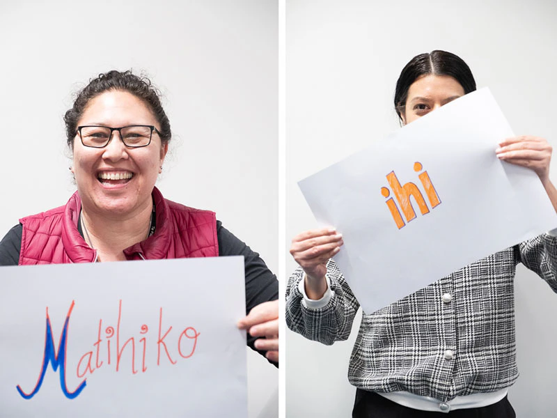 Two ladies holding up signs with Māori words 'ihi' and 'Matihiko' on them