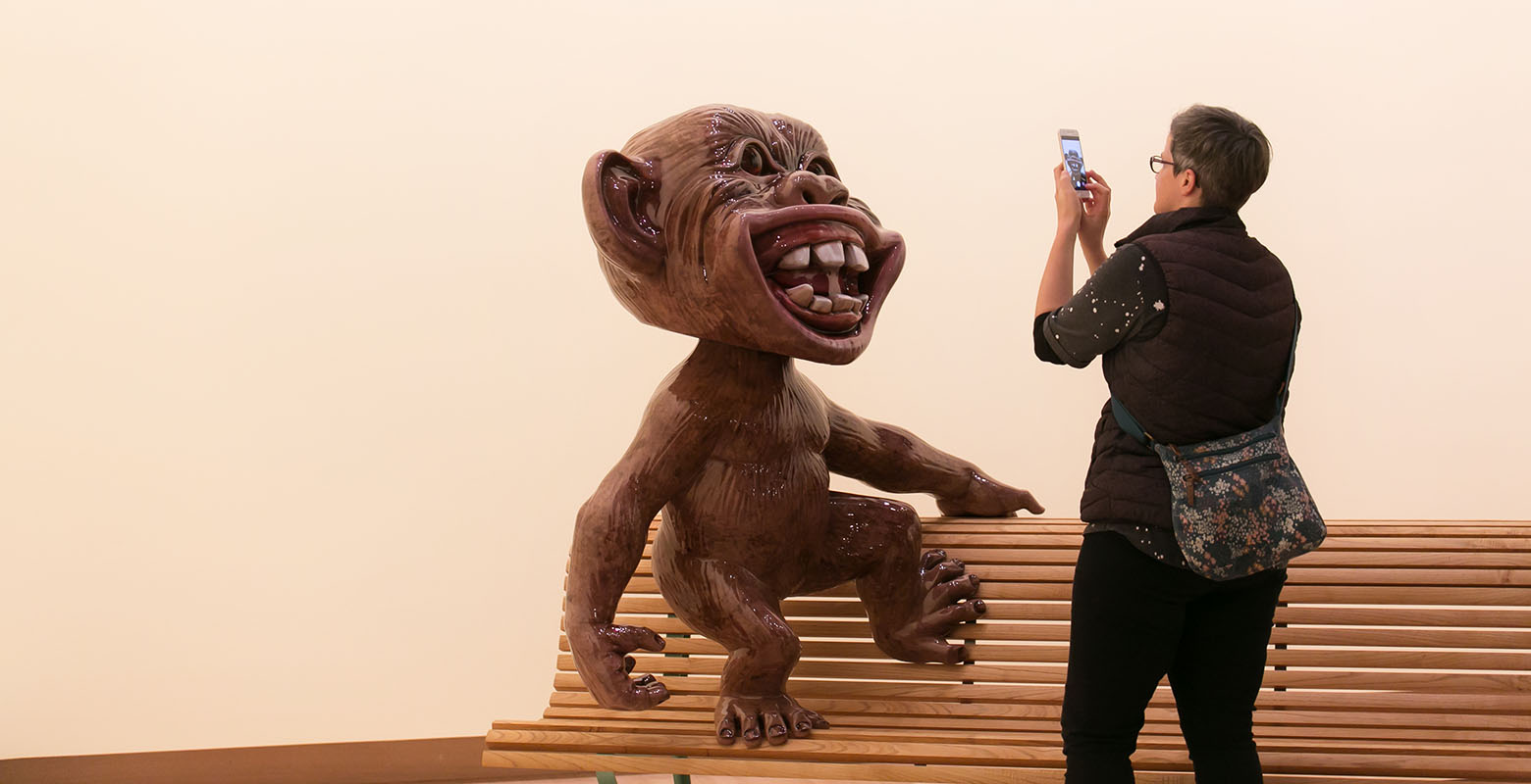 A woman takes a photo of Tiki Tour, an highly glossy sculpture of a monkey