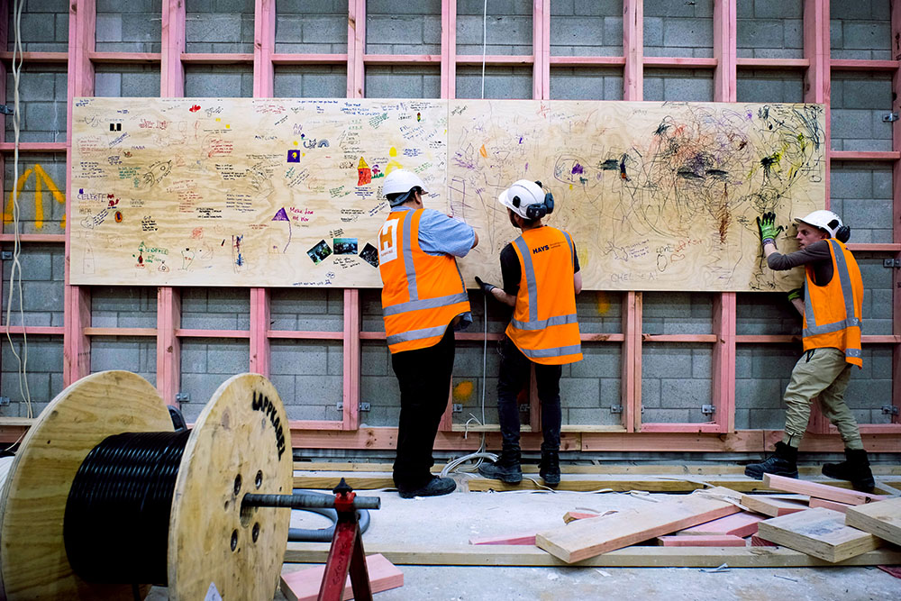 Construction workers hoist a wood panel onto the wall