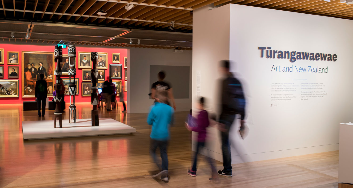 Visitors walking into the entrance of a gallery the words 'Tūrangawaewae' are on the walls