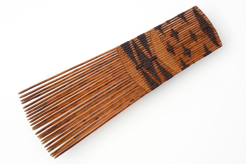 A brown wooden-looking ceremonial comb on a pale grey surface