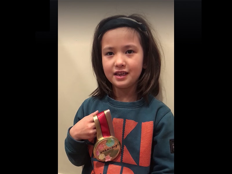 A young girl in a sweatshirt inside a house holding a homemade medal