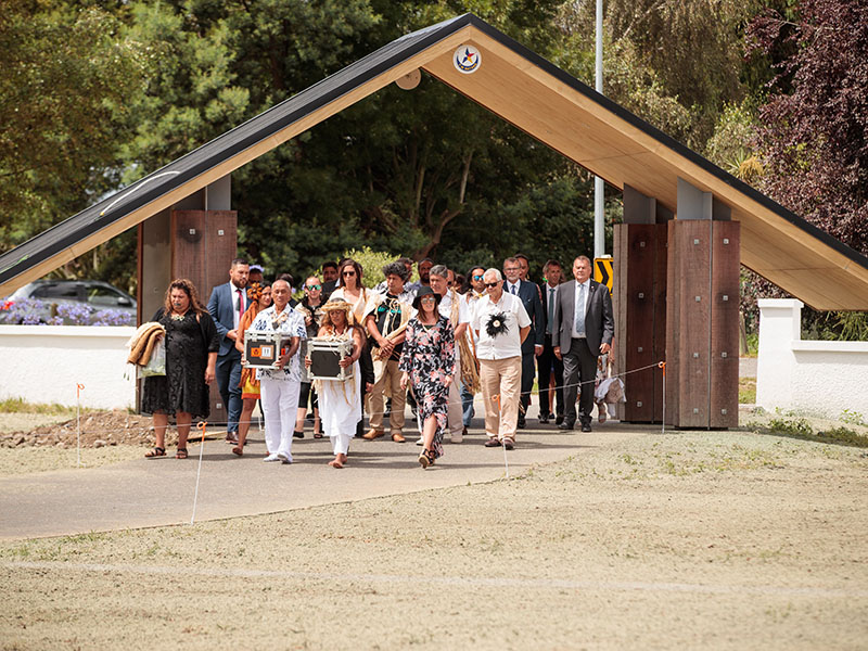 People walk through a gate along a path carrying two boxes of remains