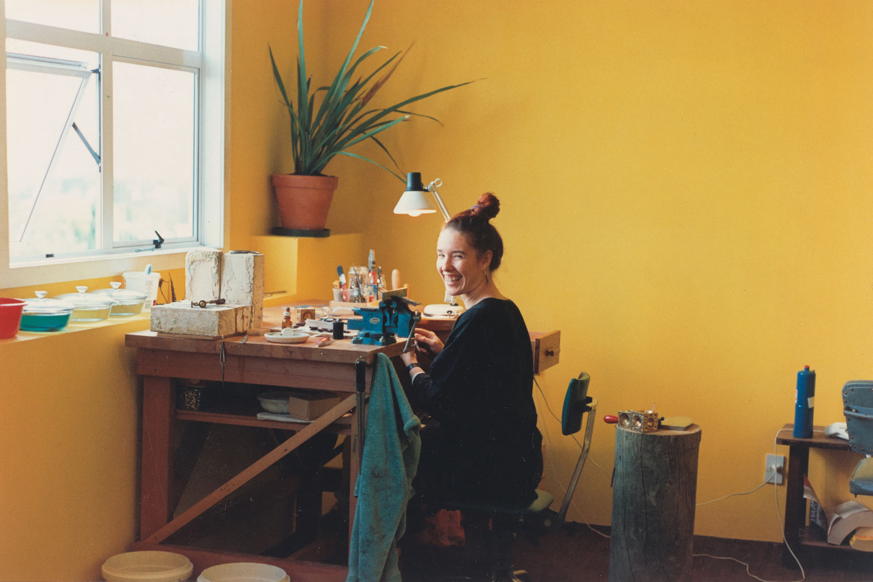 Lisa sits at desk in room with bright yellow walls crafting jewellery