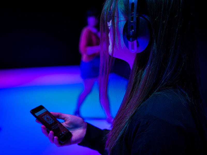 Woman looks in a room filled with colour while wearing headphones