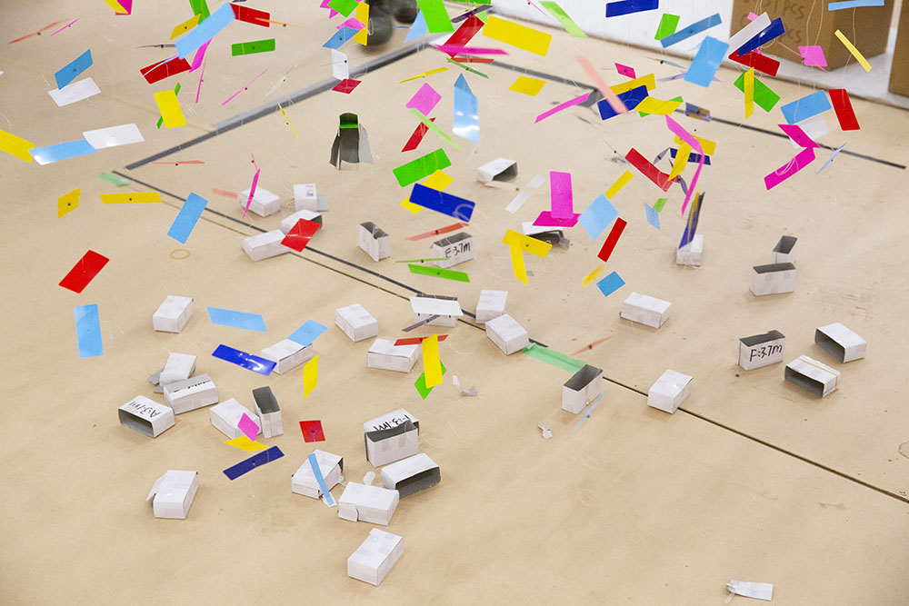 Colourful strands of Finale: Bouquet hang from the ceiling, as seen from the bottom. The boxes they came in sit underneath the strands