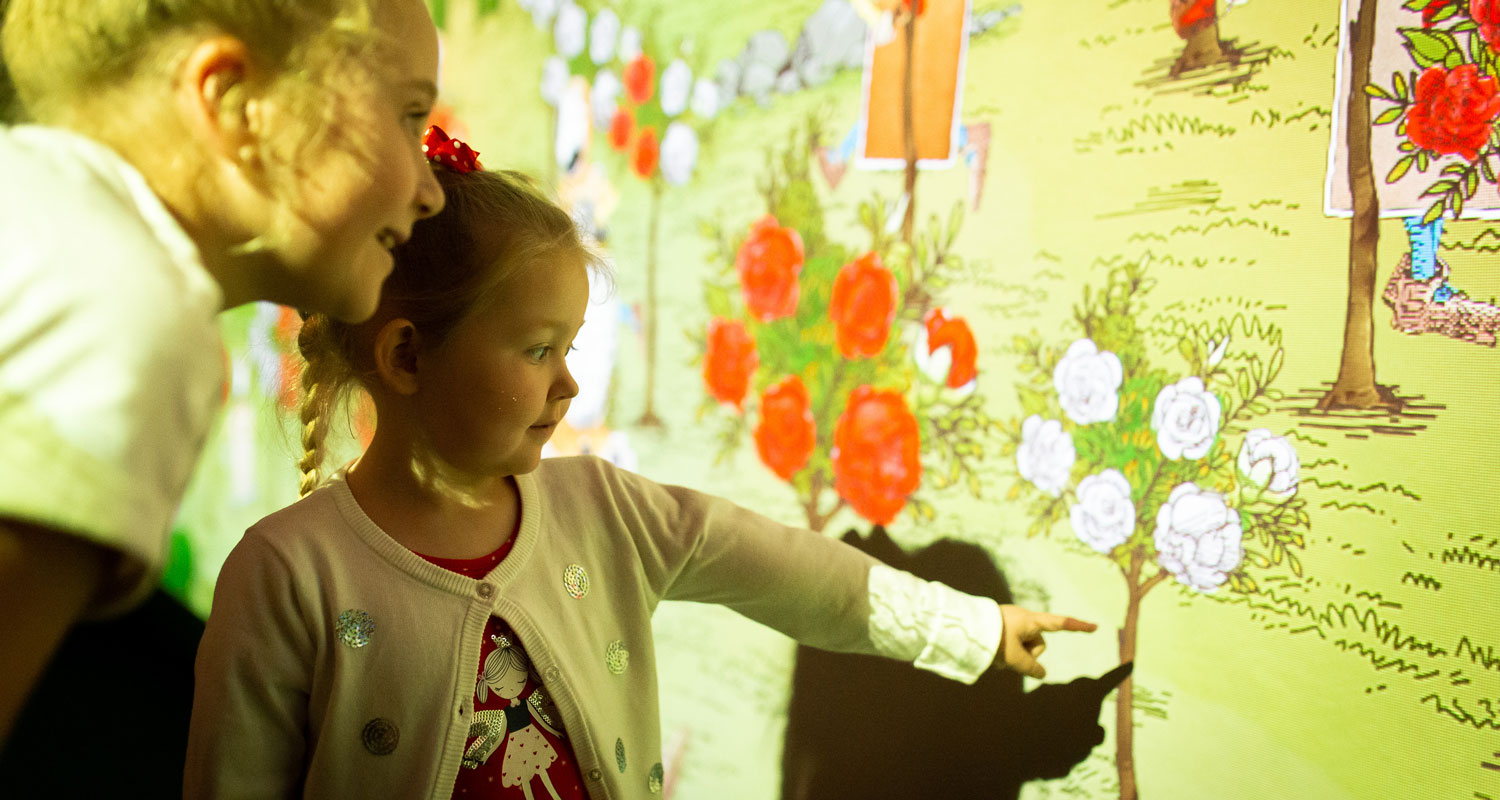 Children look at digital projections or red and white rose bushes