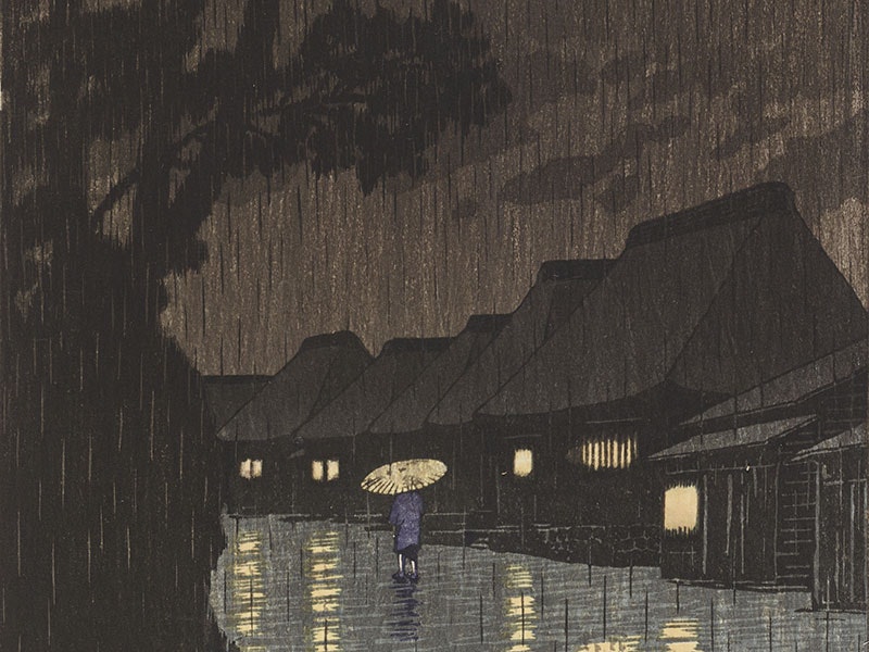 Person walks down a path in heavy rain, flanked by very tall trees on the left and houses with their lights on to the right