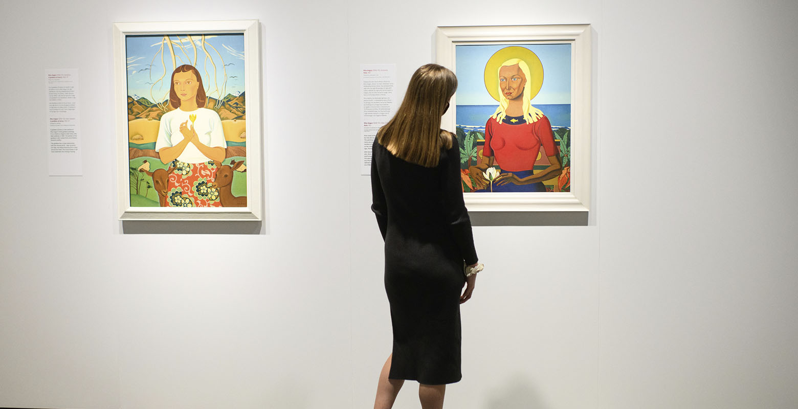 A woman stands between two paintings with her back to the camera