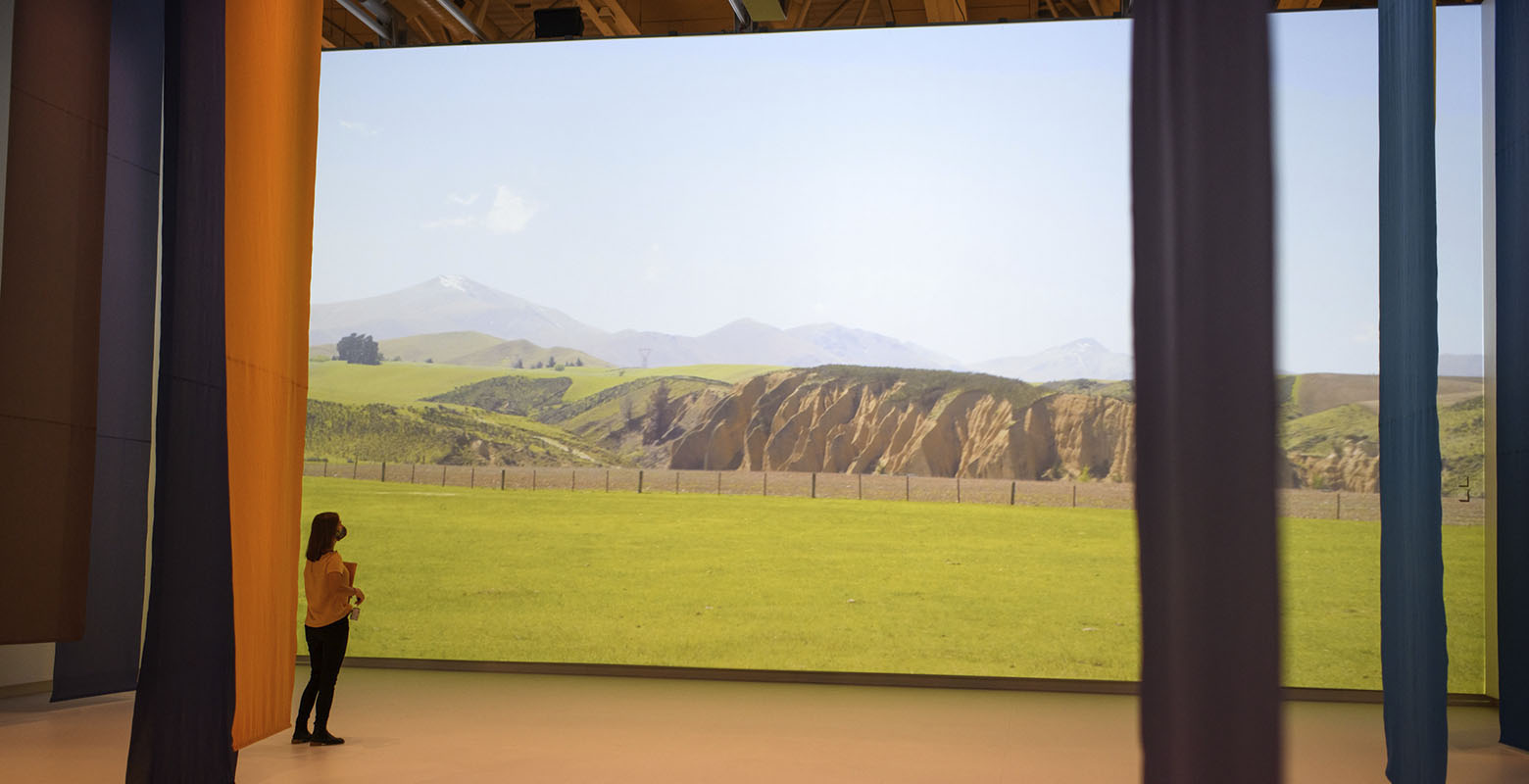 A woman stands before a giant, two-floor projection of the Central Otago landscape