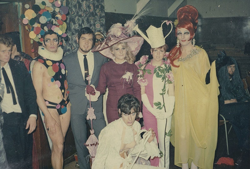 Group of people in flamboyant costume in an array of colours and styles pose for a photo