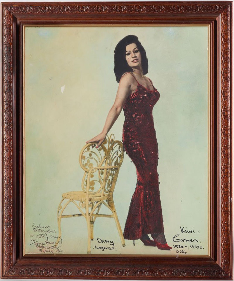 Wooden framed photo of Carmen, wearing a red sequin dress and red high heels, standing against a patio chair