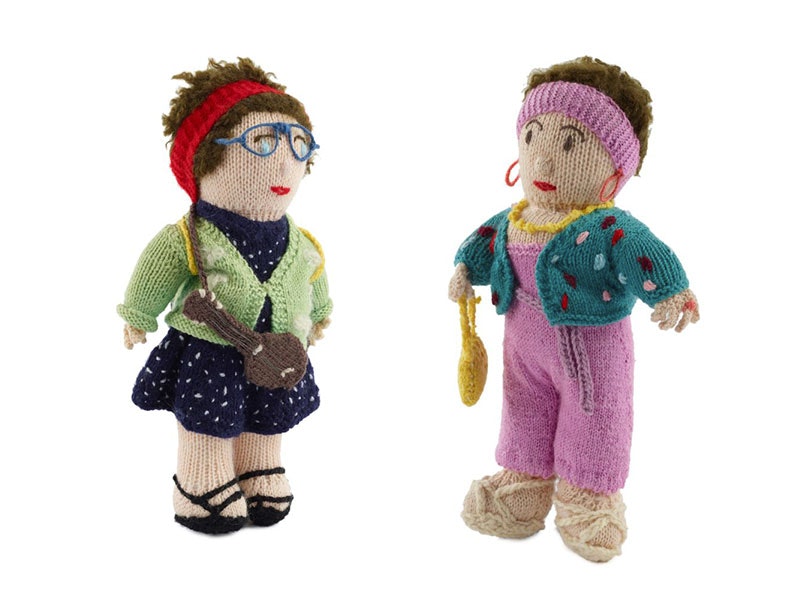Two knitted dolls. Left: A woman with a red headband, wearing glasses, in a blue dress with white polkadots and a green cardigan. On the right: A woman in pink headband and dungarees with turquoise cardigan and yellow handbag