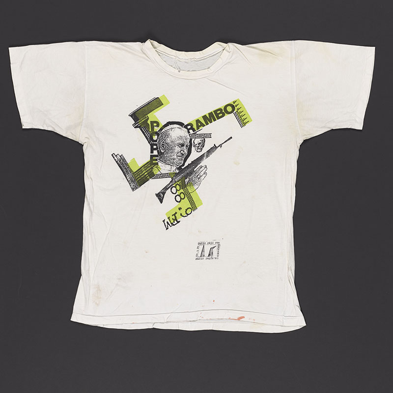 White T-shirt with a picture of Pope John Paul II and the words 'Pope Rambo' and a gun and other graphics shaped like a swastika