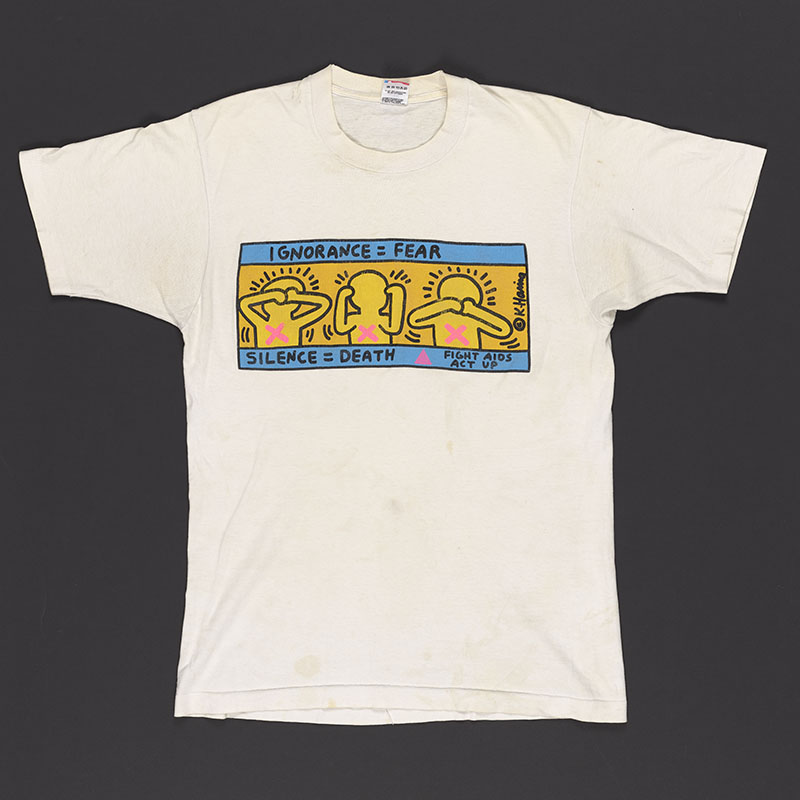 White T-shirt with a graphic on the front depicting three figures blocking their eyes, ears, and mouth in reference to 'See no evil, hear no evil, speak no evil' with 'Ignorance equals fear' written above and 'Silence equals death' written below