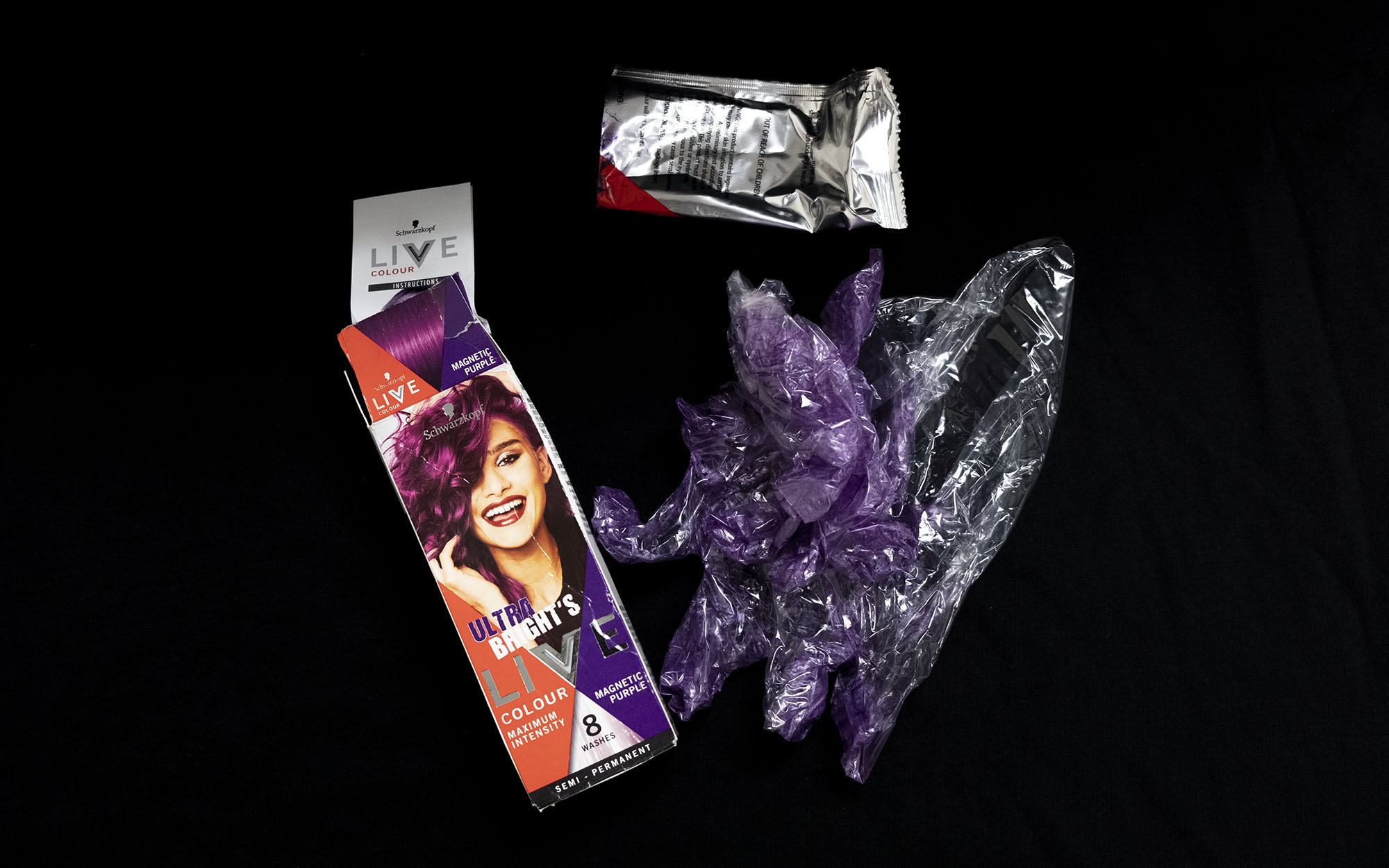 The contents of a used box of hair dye, including gloves dyed purple from application