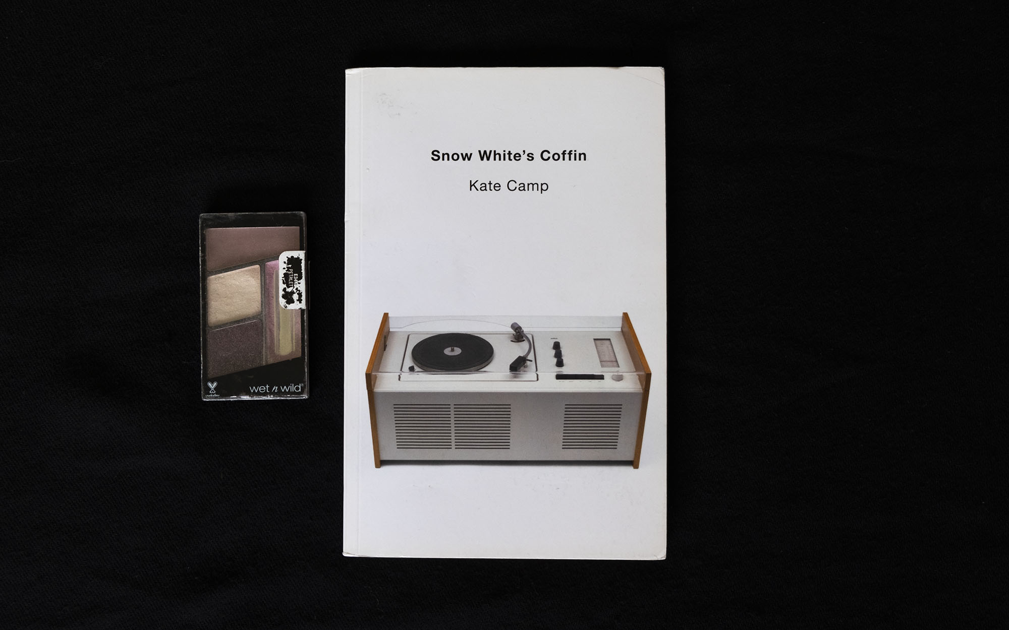 The front cover of the book Snow White’s Coffin by Kate Camp. The cover is white with a classic record player on it. Beside the book is a box of blusher