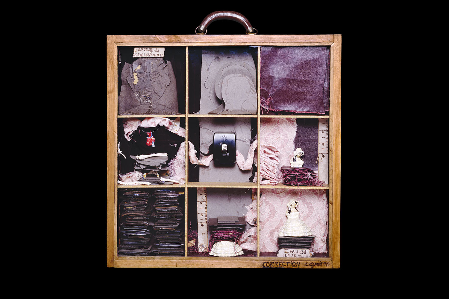 A frame resembling a suitcase divided into nine sections, containing a portrait, fabric swatches, a light switch, and various trinkets