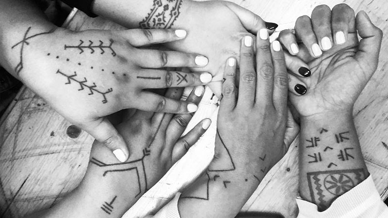 Black and white photo of five tattooed hands together