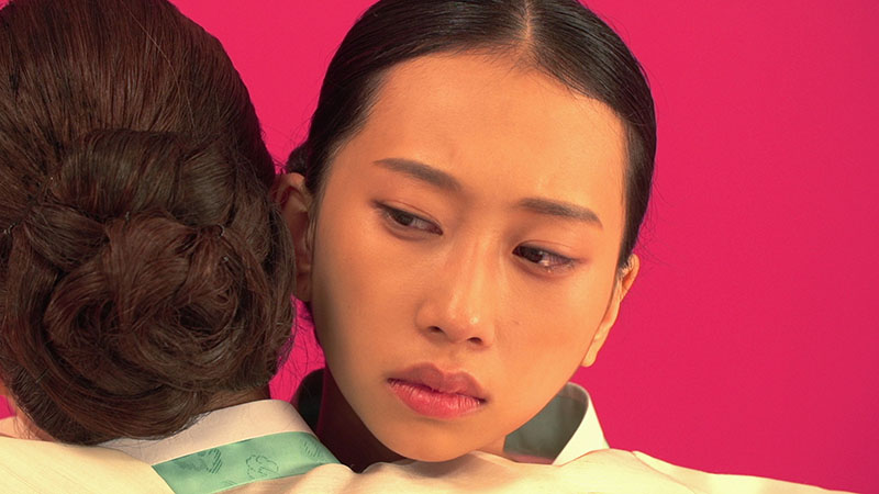 Close up of a woman’s face as she rests her head on another person’s shoulder, in a sad embrace