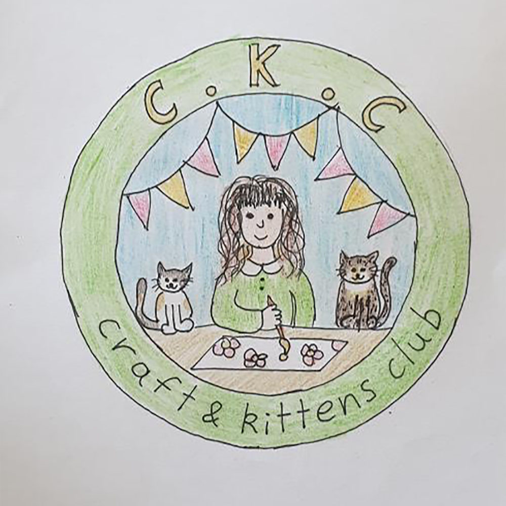 Drawing of a badge with a green circle containing the words ‘Craft and Kittens Club’. Inside the circle is a scene of a woman, wearing green, painting, flanked by two kittens. Red and yellow bunting flies above her