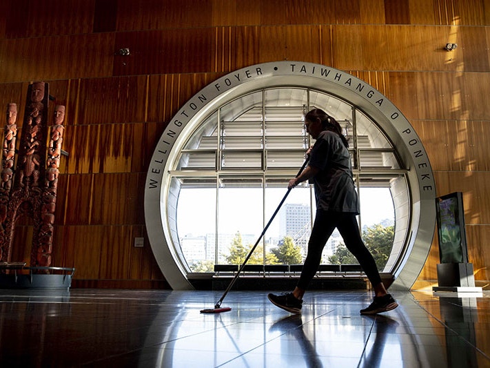 Cleaner Kellie Tapuae is one of the essential workers taking care of Te Papa while it is closed to the public. Wellington Foyer, 2020. Photo by Maarten Holl. Te Papa A woman wiping the floor passes a large round window in the Te Papa foyer
