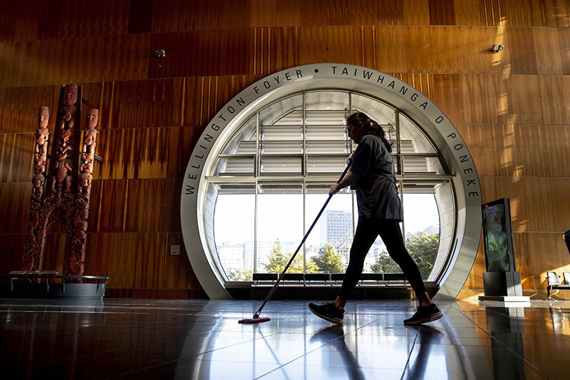 A woman wiping the floor passes a large round window in the Te Papa foyer