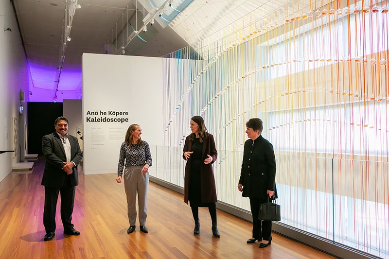 Four people stand talking in an art gallery with a large rainbow of colours behind them