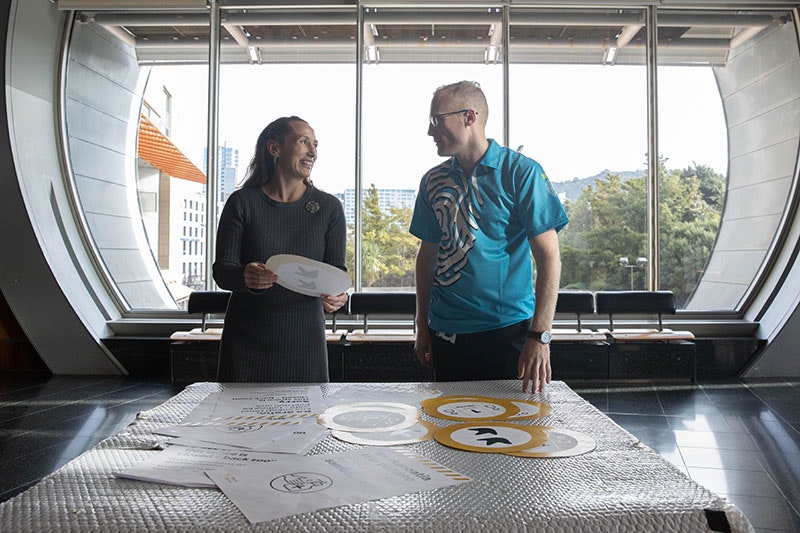 Two people stand in front of a table with an array of safety notices on it